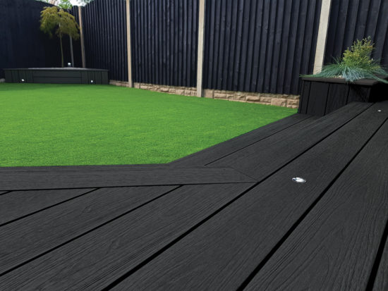 Anthrasite Black Composite Decking Swatch With Green Grass and Black Fences